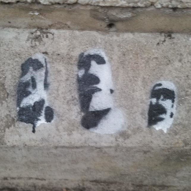 Photo of a black and white spraypainted triplet of Easter Island heads on concrete